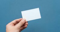 Hand holding blank white business card against blue background for mockup and branding design projects.