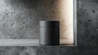 Minimalist black cylindrical speaker on concrete shelf with dramatic lighting and textured wall background creates modern aesthetic appeal.