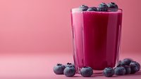 Fresh blueberry smoothie in glass with whole berries on pink background. Healthy breakfast drink rich in antioxidants and vitamins for wellness lifestyle.