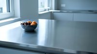 Modern minimalist kitchen with stainless steel countertop and black bowl of fresh fruit. Bright natural light from window illuminates clean, contemporary interior design space.