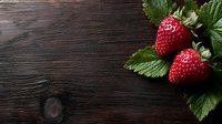 Fresh ripe strawberries with green leaves on dark rustic wooden background with copy space for text, top view composition for food photography.