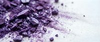 Crushed purple eyeshadow and powder scattered on white surface, suitable for cosmetics, beauty, and makeup product photography.