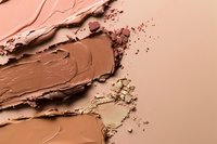 Smeared and crushed makeup foundation samples in nude and brown tones on beige background, showing texture and consistency of cosmetic products.