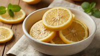 Fresh lemon slices arranged in a rustic ceramic bowl on a wooden table with mint leaves, showcasing vibrant citrus texture for food blogs.