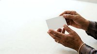 Close-up of hands holding blank white card or envelope against neutral background, suitable for business communication, greeting card mockups, and corporate messaging designs.