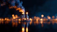 Industrial chimneys emitting smoke against night sky with blurred city lights reflecting on water surface, creating atmospheric urban landscape with bokeh effect.