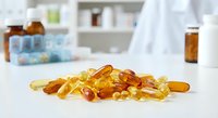 Omega-3 fish oil capsules scattered on white surface in modern pharmacy setting with medicine bottles and healthcare products in blurred background.