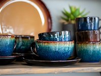 Handcrafted ceramic dinnerware set with blue-green glazed bowls and plates on wooden shelf. Artisan pottery collection for modern kitchen dining decor.