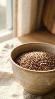 Organic flax seeds in rustic ceramic bowl on natural linen fabric near window with warm sunlight for healthy cooking and nutrition concepts.