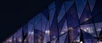 Modern glass facade with geometric triangular panels reflecting night sky and city lights, suitable for corporate, architecture, and technology design projects.