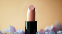 Nude pink lipstick on blurred floral background with soft bokeh effect creates romantic feminine composition for beauty and cosmetic marketing.