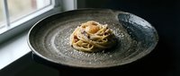 Elegant spaghetti carbonara served on a rustic ceramic plate, topped with egg yolk, crispy pancetta, and grated parmesan in moody restaurant lighting.