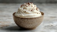 Creamy whipped dessert topped with chocolate shavings served in rustic ceramic bowl on concrete surface, soft natural lighting creates appetizing mood.