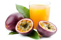 Fresh passion fruits with one cut in half showing seeds and pulp next to glass of tropical juice on white background, for food and beverage marketing.