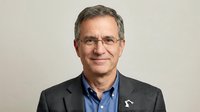 Middle-aged man with gray hair and glasses wearing dark blazer over blue shirt, professional headshot for corporate, business, or executive use.