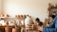 Artisan potter holding smooth clay vessel in hands during ceramic workshop, showcasing handmade pottery craftsmanship and traditional clay working techniques for creative studio environments.