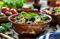 Fresh pasta salad with black olives, cherry tomatoes and basil leaves in rustic ceramic bowl, Mediterranean cuisine style food photography.