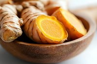Fresh turmeric root and sliced pieces in wooden bowl showing bright orange flesh, natural healing spice ingredient for cooking and wellness recipes.