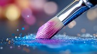 Makeup brush dipped in pink pigment touching blue glitter surface with bokeh lights background, creating artistic cosmetic powder splash effect.