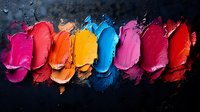 Colorful lipstick smears in vibrant shades creating artistic makeup palette on dark textured background for cosmetic and beauty industry designs.