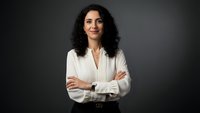 Confident Middle Eastern businesswoman with crossed arms wearing white blouse against dark background for corporate and professional marketing materials.