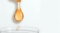 Golden honey dripping from wooden spoon into glass bowl on white background. Natural sweetener ingredient for cooking, baking and healthy nutrition.