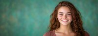 Young Caucasian woman with natural wavy brown hair and bright genuine smile wearing casual burgundy top against blurred teal background, panoramic portrait format.