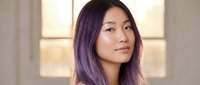 Young Asian woman with purple ombre hair looking confidently at camera in modern indoor setting with natural lighting for lifestyle content.