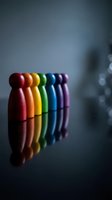 Colorful wooden peg figures in rainbow colors standing in row on reflective surface representing diversity, teamwork and inclusion concepts.