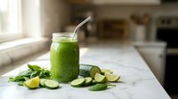 Fresh green smoothie in glass jar with straw surrounded by spinach leaves and lime slices on white marble kitchen counter for healthy lifestyle.