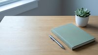 Minimalist workspace with green notebook, pen and succulent plant on wooden desk near window. Clean office setup for productivity and planning.