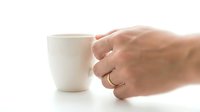Hand holding white ceramic coffee mug on clean background. Morning beverage concept for kitchen and dining designs. Isolated cup ready for commercial use.