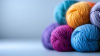 Colorful yarn balls in vibrant shades of blue, purple, orange, and turquoise arranged on light background with soft focus effect, showcasing texture and crafting materials.