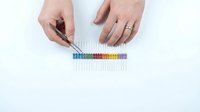 Hands arranging colorful resistors in a rainbow row on white background using tweezers, electronics hobby and DIY circuit project concept.