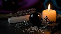 Mystical fortune telling setup with burning candle, crystal ball, pentagram pendant and tarot cards on dark surface for spiritual divination practices.