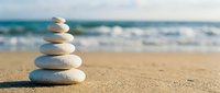 Balanced stack of smooth white stones on sandy beach with ocean waves in background creating peaceful zen meditation scene for wellness and mindfulness concepts.