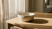 Minimalist ceramic bowl on wooden table with natural sunlight creating soft shadows in modern interior space for home decor and lifestyle concepts.