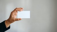 Close-up of male hand holding blank white business card against neutral background, suitable for corporate branding and professional presentations.