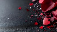 Red heart-shaped confetti and ribbon scattered on dark textured surface for romantic celebrations, Valentine's Day decorations and love themes.