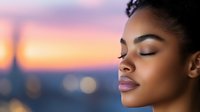 Young African American woman with closed eyes and serene expression against blurred sunset cityscape background with bokeh lights, showcasing natural makeup and peaceful mindfulness.