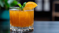 Fresh orange cocktail garnished with citrus slice and mint leaves in crystal glass on dark background, fizzy drink with bubbles and ice cubes.