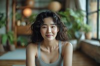 Young Asian woman with wavy hair smiling in cozy home interior with plants and natural light, creating warm atmosphere for lifestyle content.
