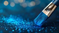 Artistic paintbrush with blue glitter particles on dark background with bokeh lights creates magical atmosphere for creative design projects.