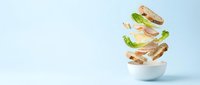 Fresh sandwich ingredients floating above white bowl with lettuce, tomato, cheese, meat and bread slices on light blue background for food design.