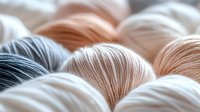 Soft wool yarn balls in gentle pastel peach, white and gray colors arranged in rows creating cozy textile background pattern for knitting and crafting projects.