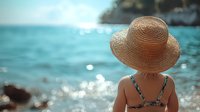 Woman in straw hat enjoying peaceful moment at turquoise ocean beach with sparkling water reflections and rocky coastline creating serene vacation atmosphere.