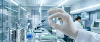 Scientist in white lab coat and gloves holding petri dish in modern laboratory with colleagues working in background, suitable for biotech, pharmaceutical, and medical research projects.