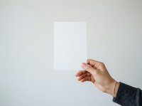 Person of medium skin tone holding blank white card or paper against neutral background, suitable for mockups, presentations, advertising campaigns, and marketing materials.