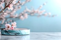 Delicate pink cherry blossoms above marble podium on soft blue background. Minimal spring composition with selective focus creates serene spa atmosphere.