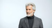 Mature man with white hair and beard, wearing gray blazer and black turtleneck, isolated on white background for corporate, business, and professional design applications.